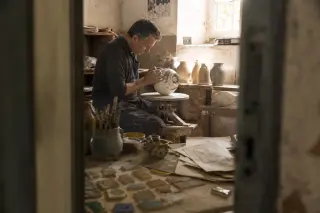Artisan shaping faience on a pottery wheel in a Quimper museum workshop, surrounded by clay tools and test tiles in warm, natural morning light.
