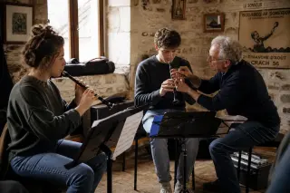 Musicians in a rustic Breton rehearsal room, practicing together, surrounded by music stands and cases, with soft afternoon light creating a warm, authentic atmosphere.